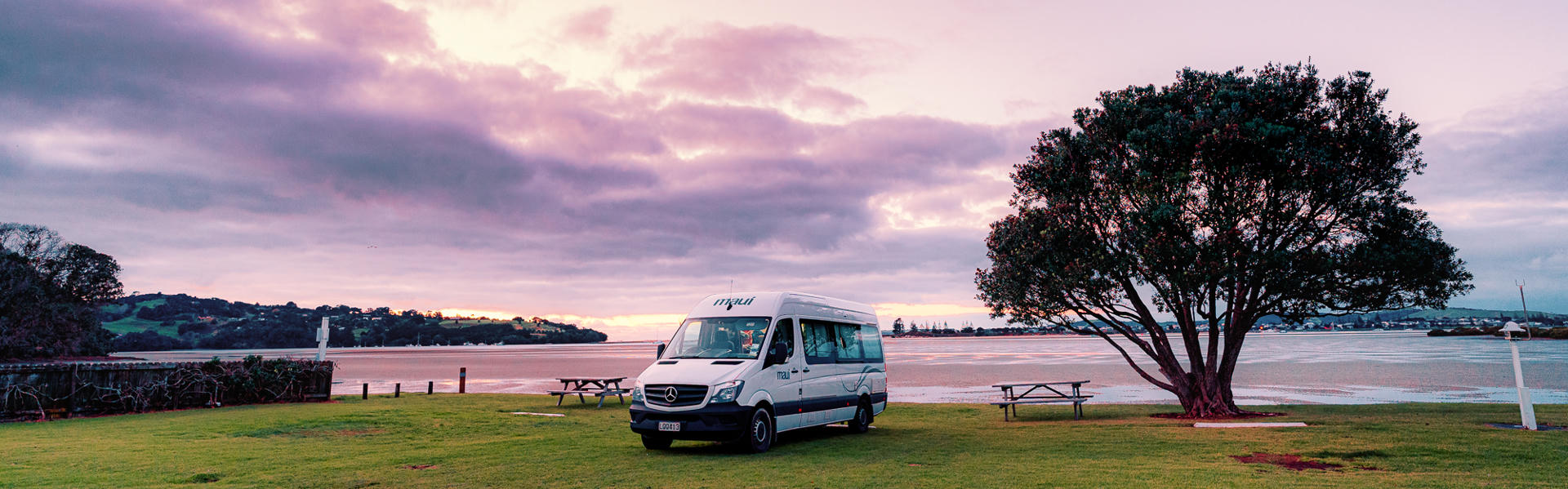 Ultima von Maui Motorhomes neben Baum vor See in Australien bei rötlichem Licht