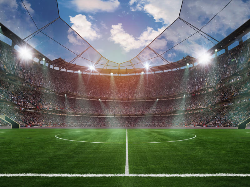 Ein vollbesetztes Fußballstadion mit beleuchtetem Spielfeld und Zuschauerrängen vor dem Spielbeginn.