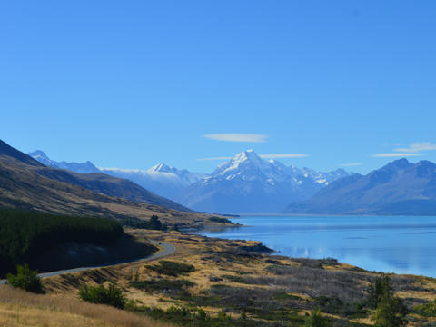 Eine gewundene Straße führt am Lake Pukaki in Neuseeland entlang in verschneite Berge